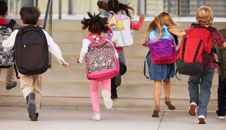 children running in to school with their backpacks children running in to school with their backpacks