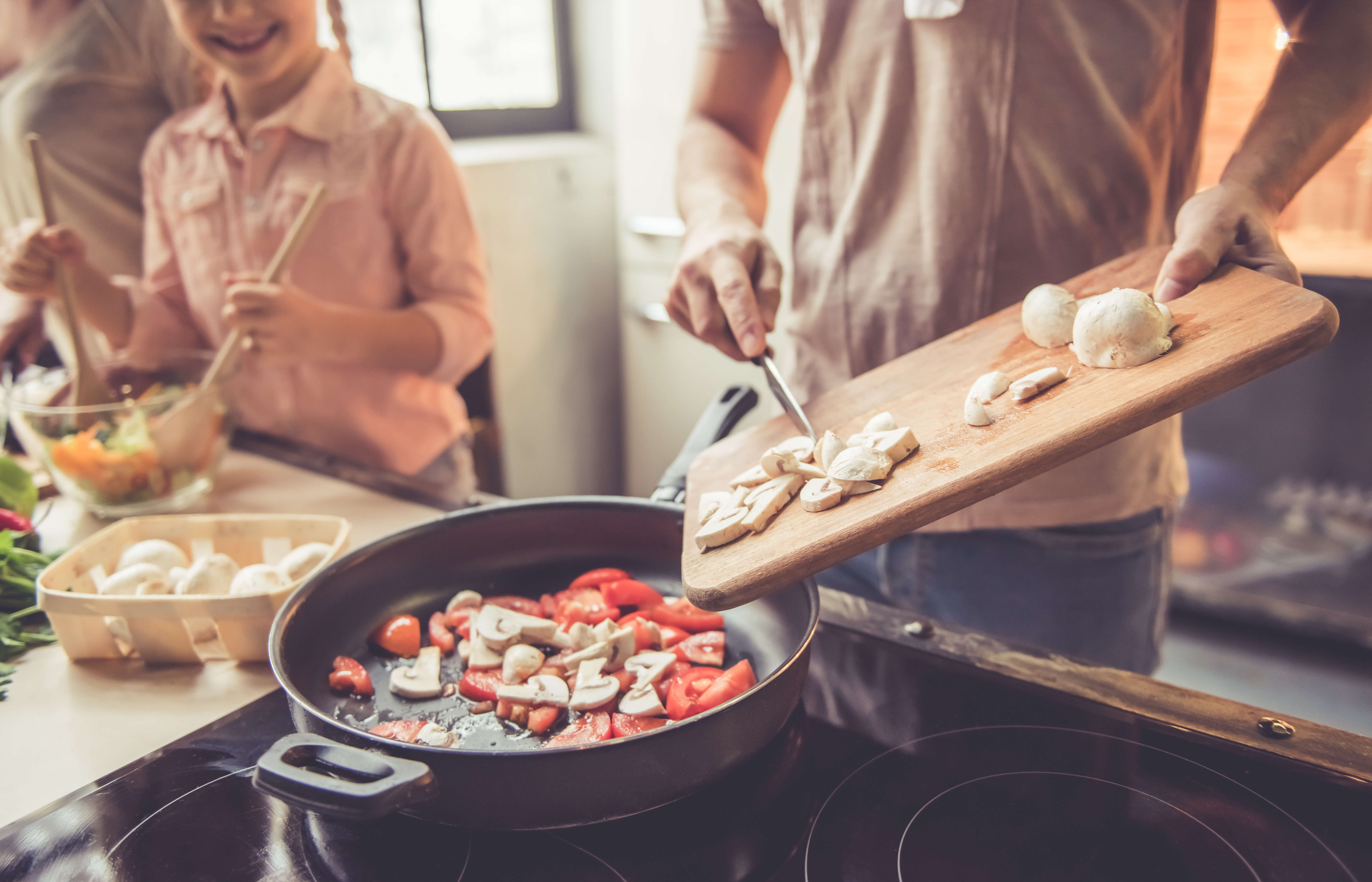 Man and child cooking together putting mushrooms in a pan