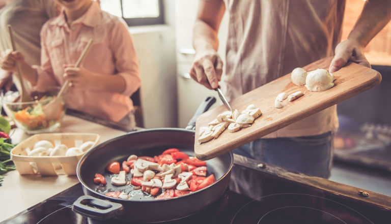 Man and child cooking together putting mushrooms in a pan Man and child cooking together putting mushrooms in a pan