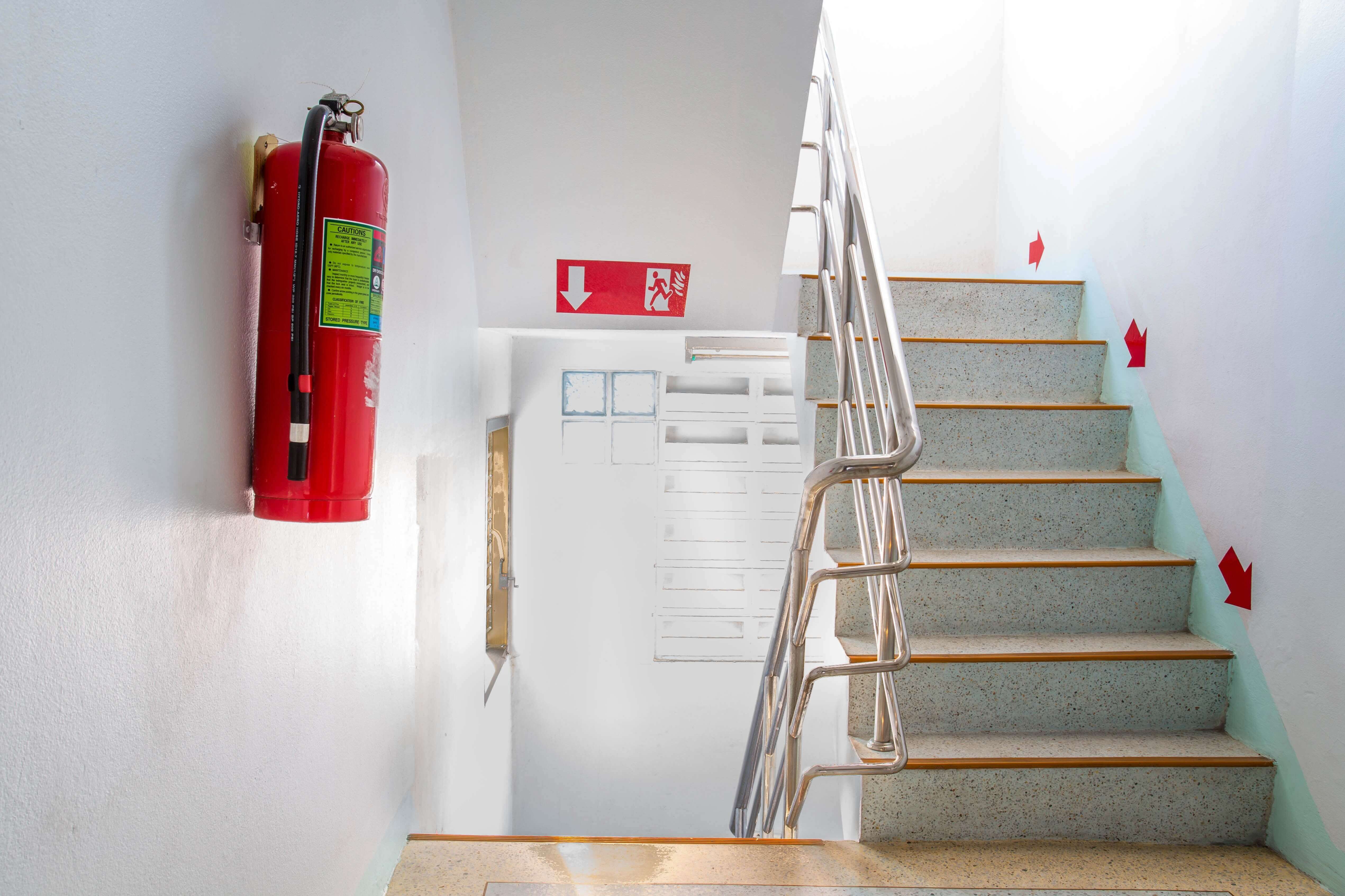 staircase with white walls leading to a evacuation door with red fire extinguisher on the wall