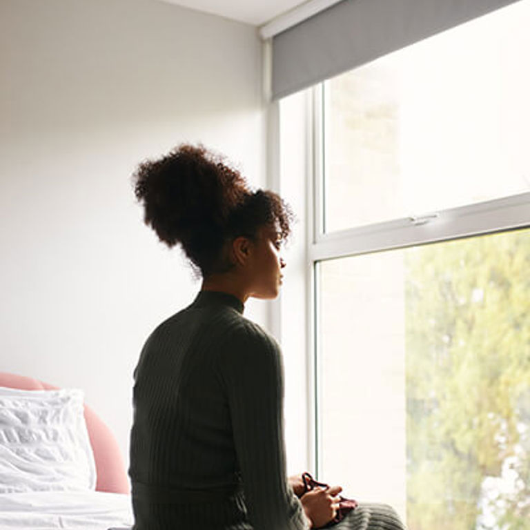 woman sitting on her bed looking out the window woman sitting on her bed looking out the window