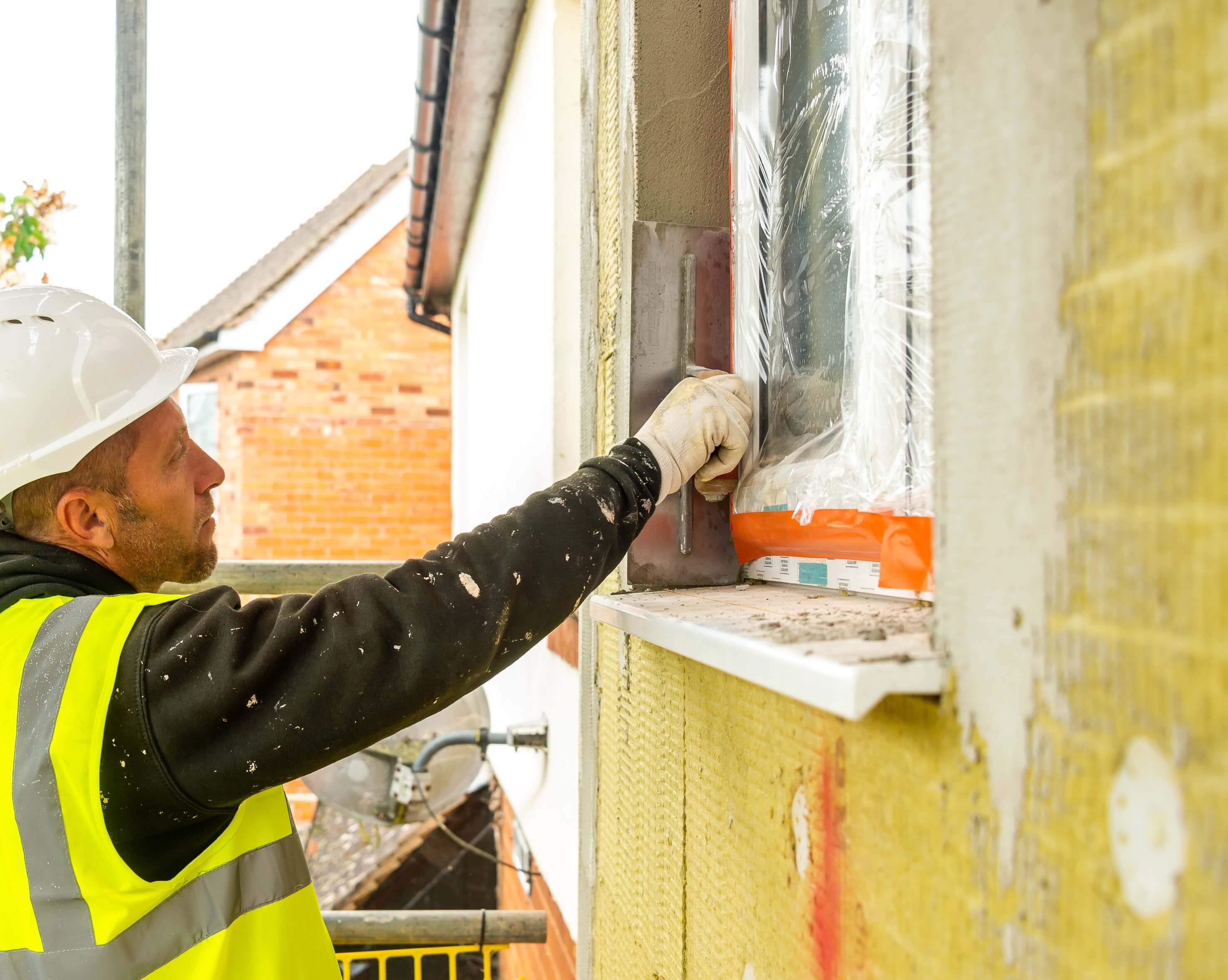 man in yellow reflective shirt insulating a window