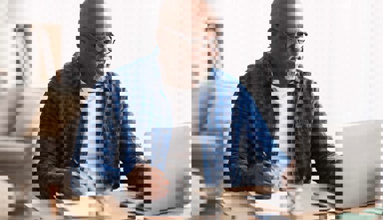 image of man in a blue shirt using a laptop and writing on a notepad image of man in a blue shirt using a laptop and writing on a notepad