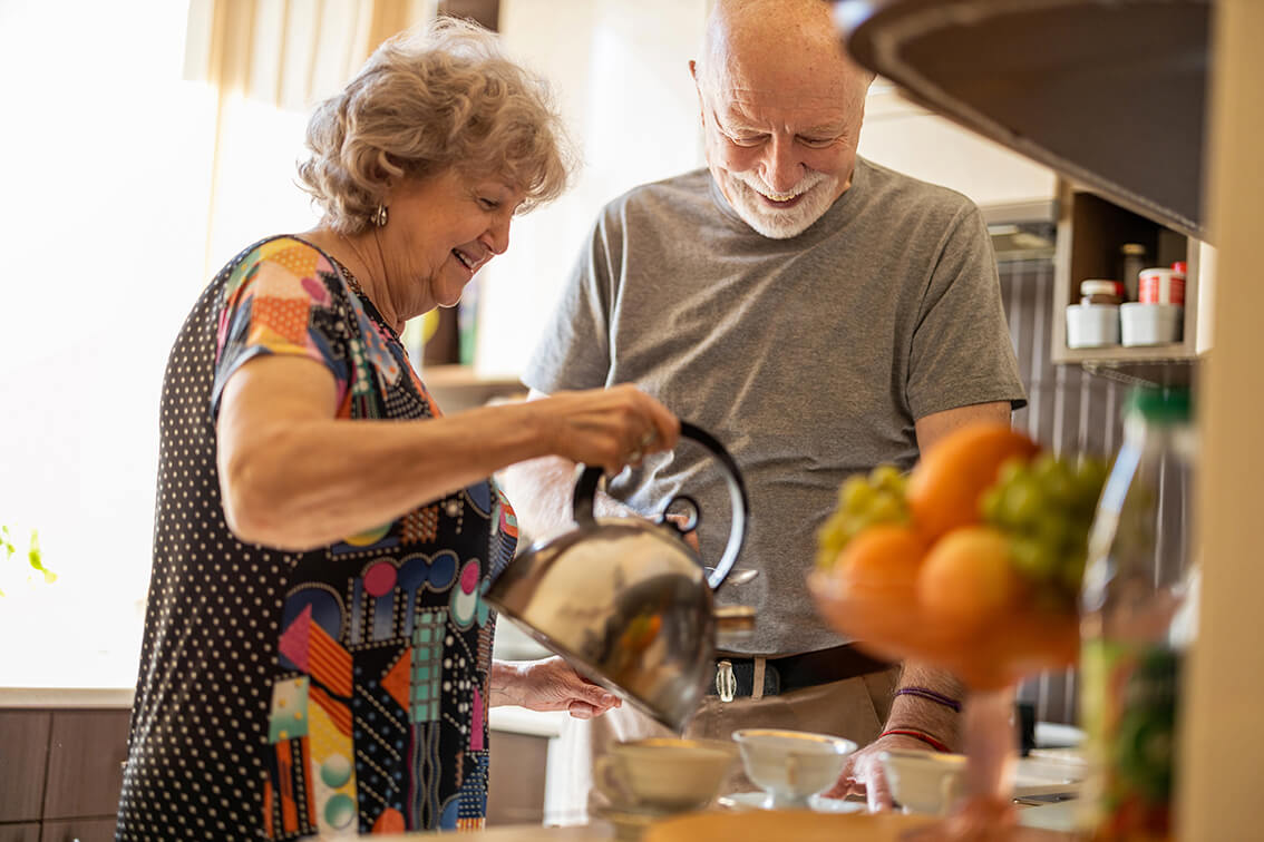 elderly woman pouring water from a kettle in the cup with a elderly man