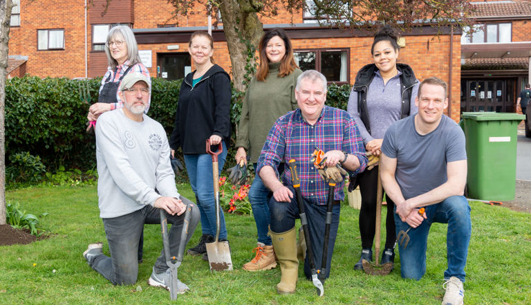 seven people on a green lawn smiling holding garden tools seven people on a green lawn smiling holding garden tools