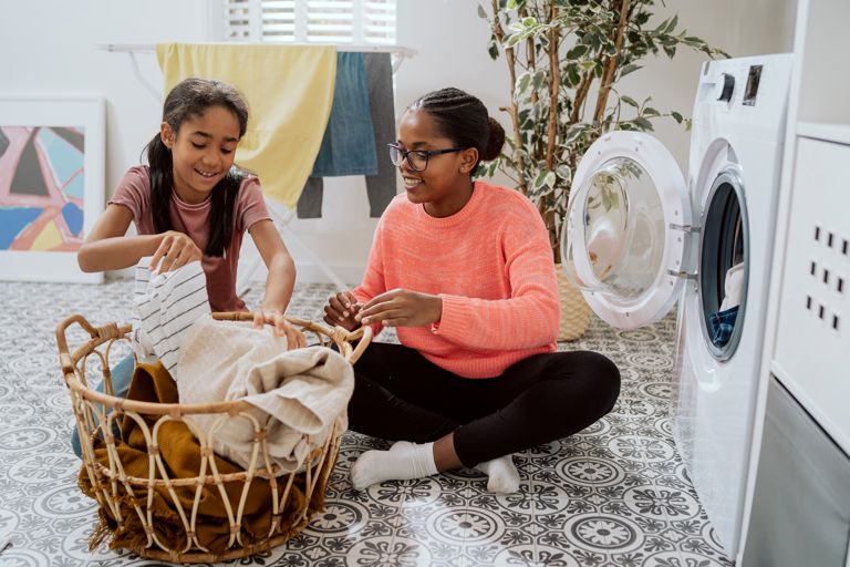 Two girls sat on the floor putting clothes into a washing machine Two girls sat on the floor putting clothes into a washing machine